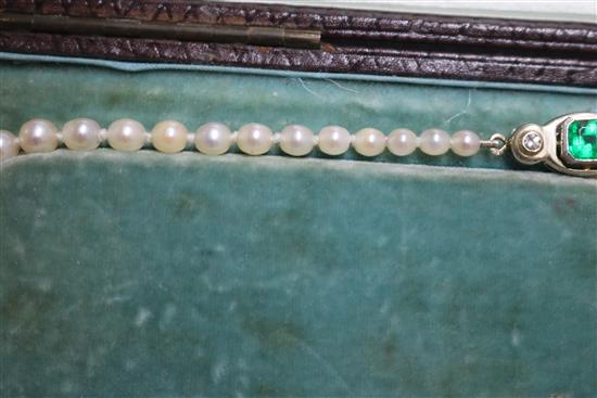 A single strand graduated cultured pearl necklace with an emerald and diamond set white metal clasp, approx. 35cm.